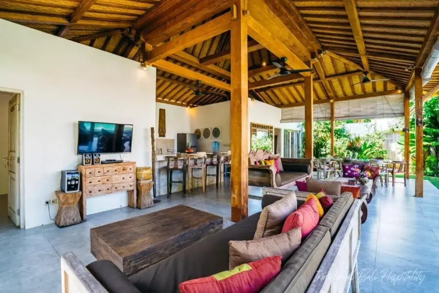 The open living pavilion — carved teak columns, deep sofas, the garden on every side