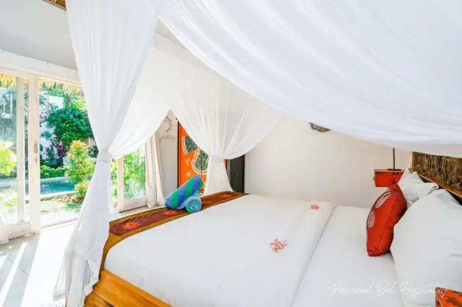 A canopy bed in white netting, the pool visible through the bedroom doors