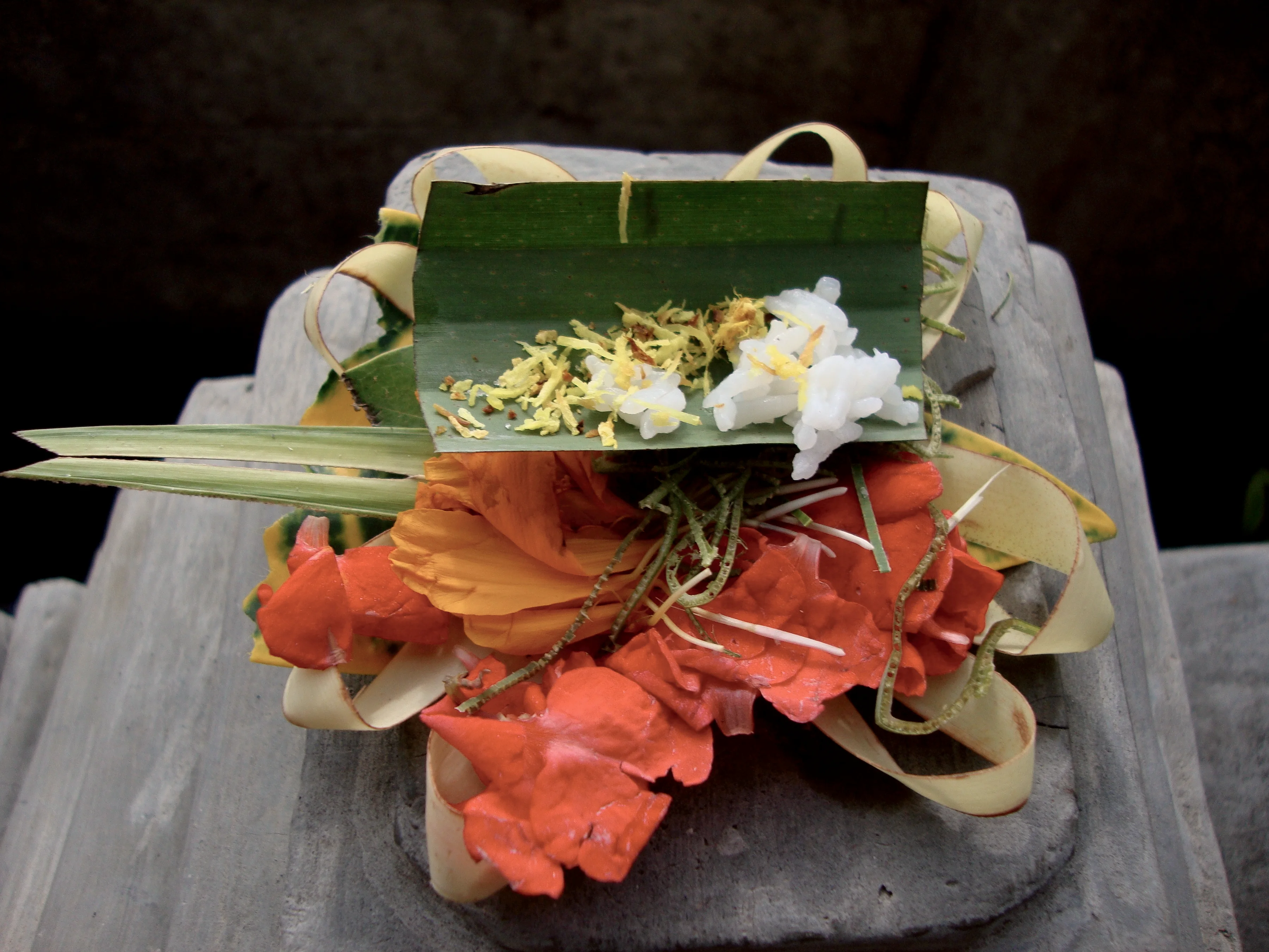 A canang sari offering of flowers in a palm-leaf tray