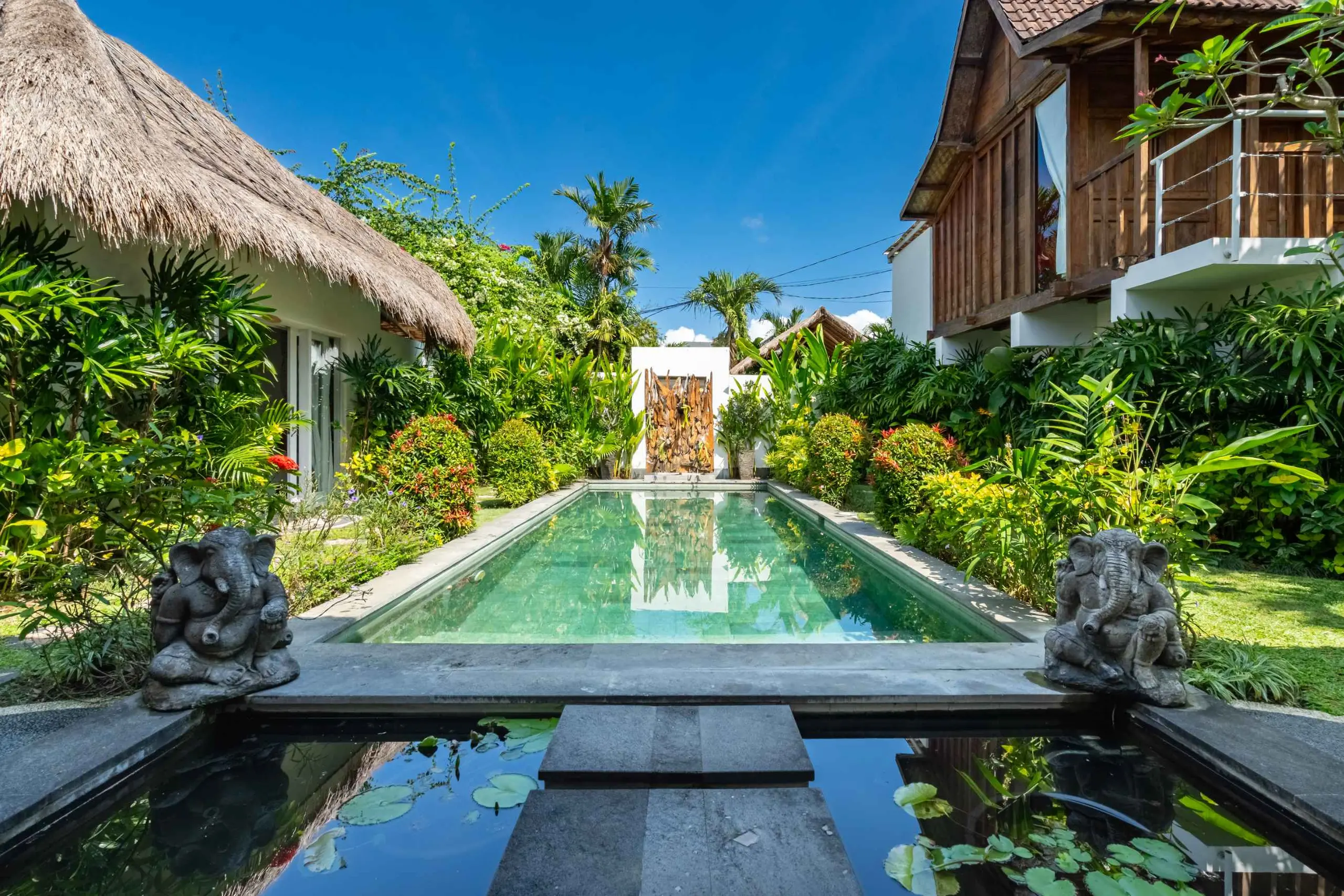 The long pool flanked by stone guardians, morning light through the palms