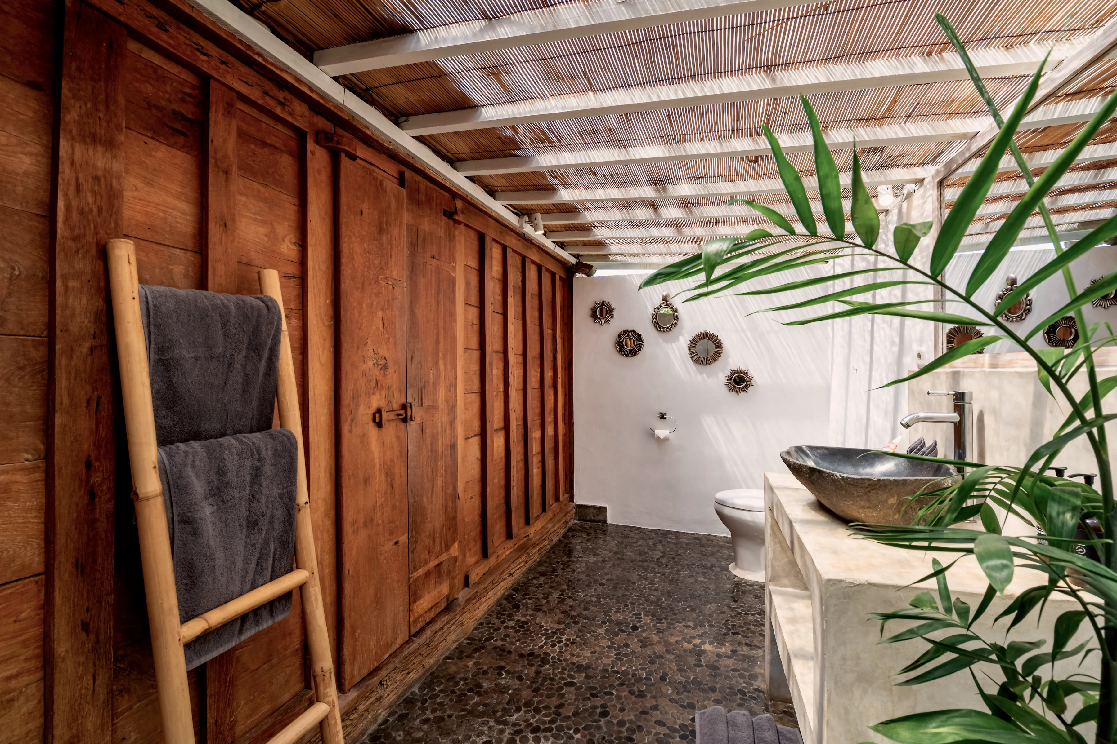 The Joglo bedroom’s open-air bathroom: a stone basin beside the teak wall