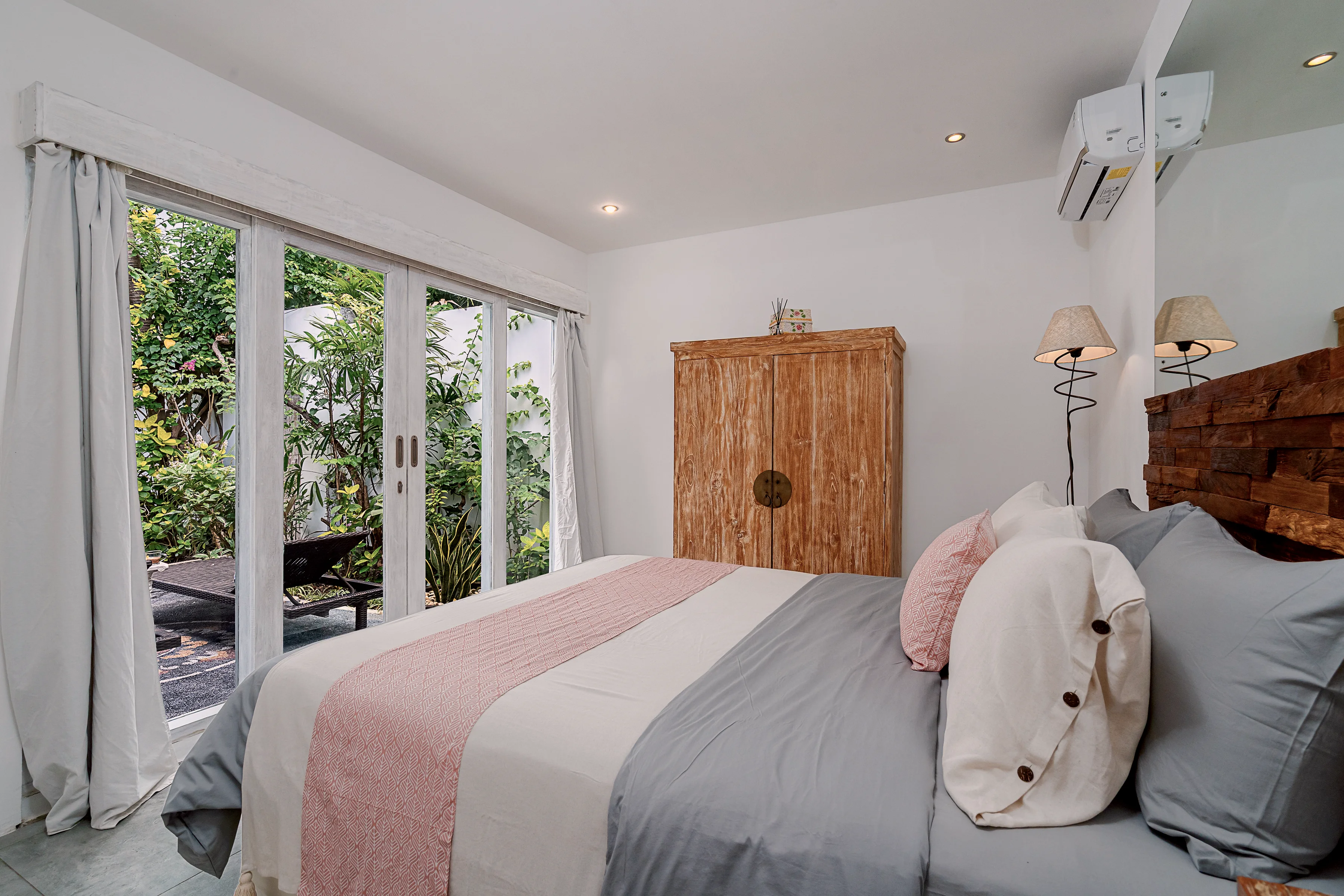 A garden bedroom: pink and grey linen, a carved wardrobe and doors to the garden