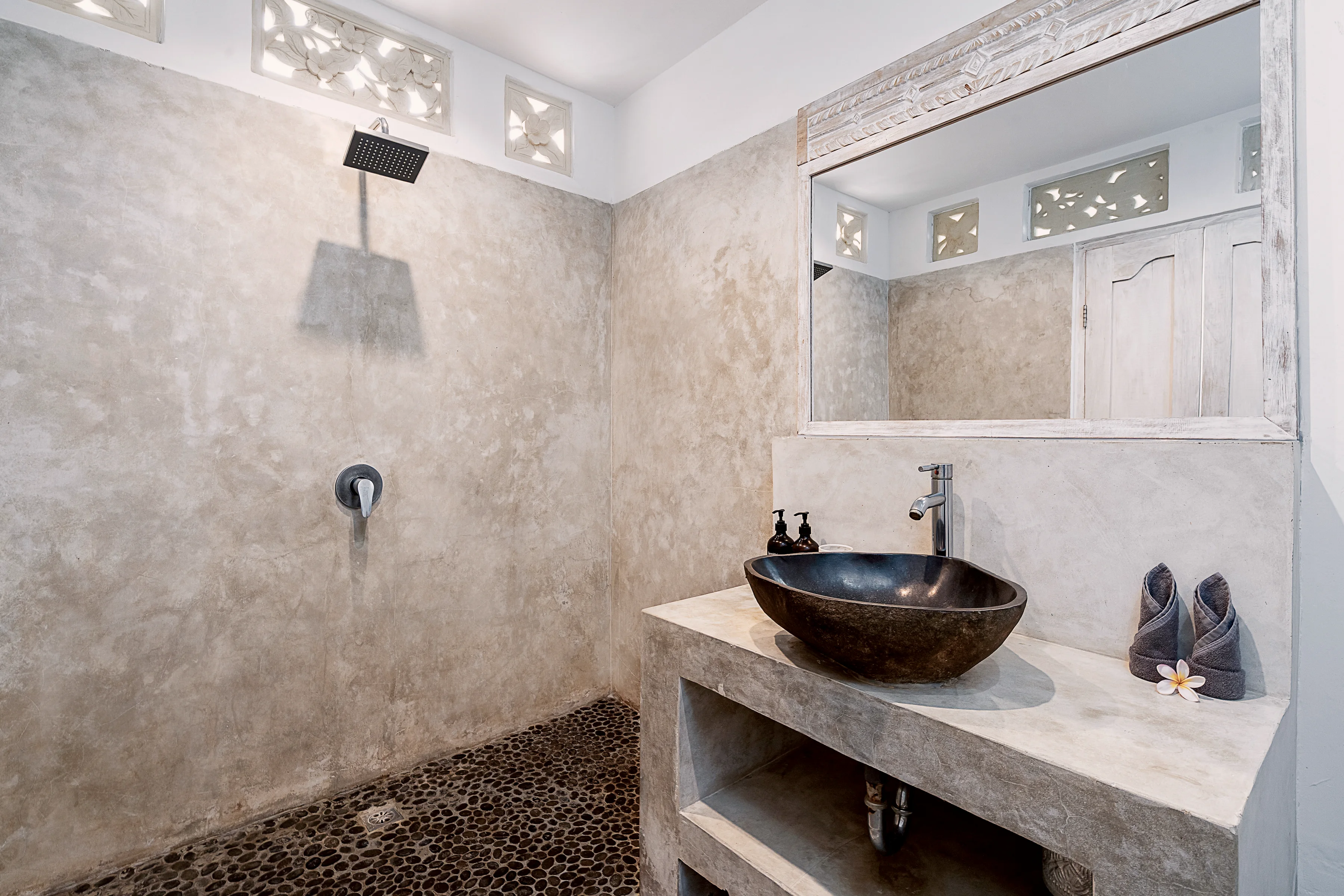 A bathroom with a rain shower and a stone basin on a concrete vanity