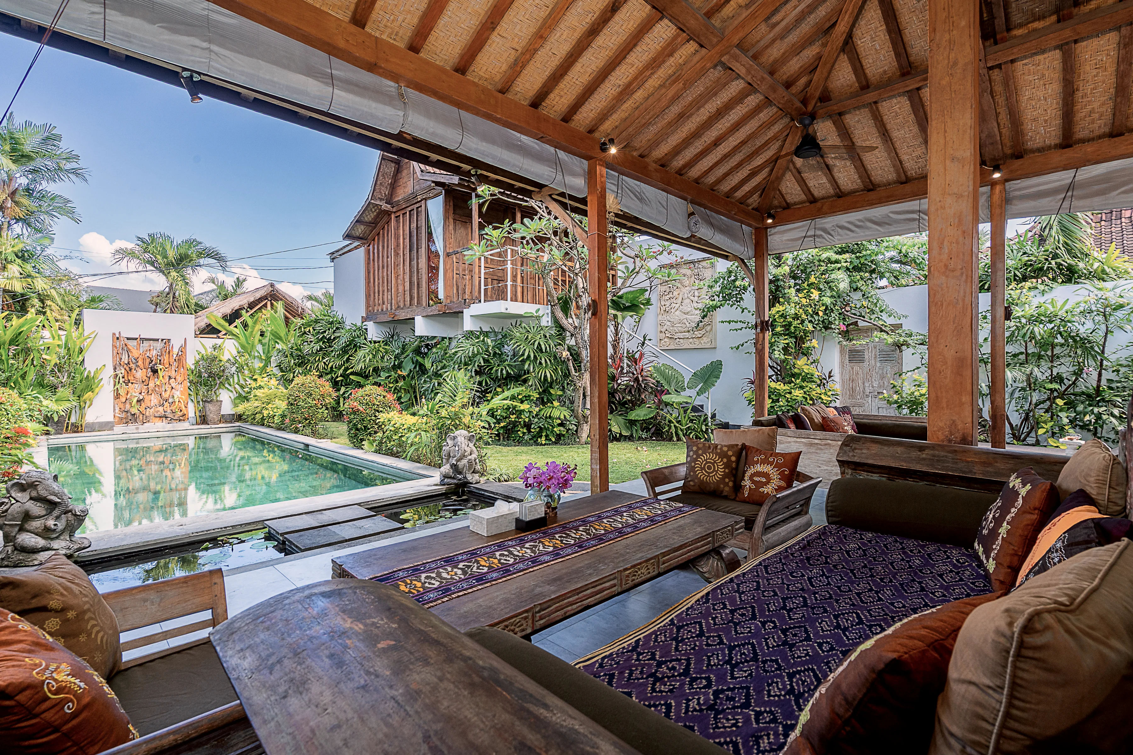 Daybeds under the pavilion with the pool and the teak house beyond