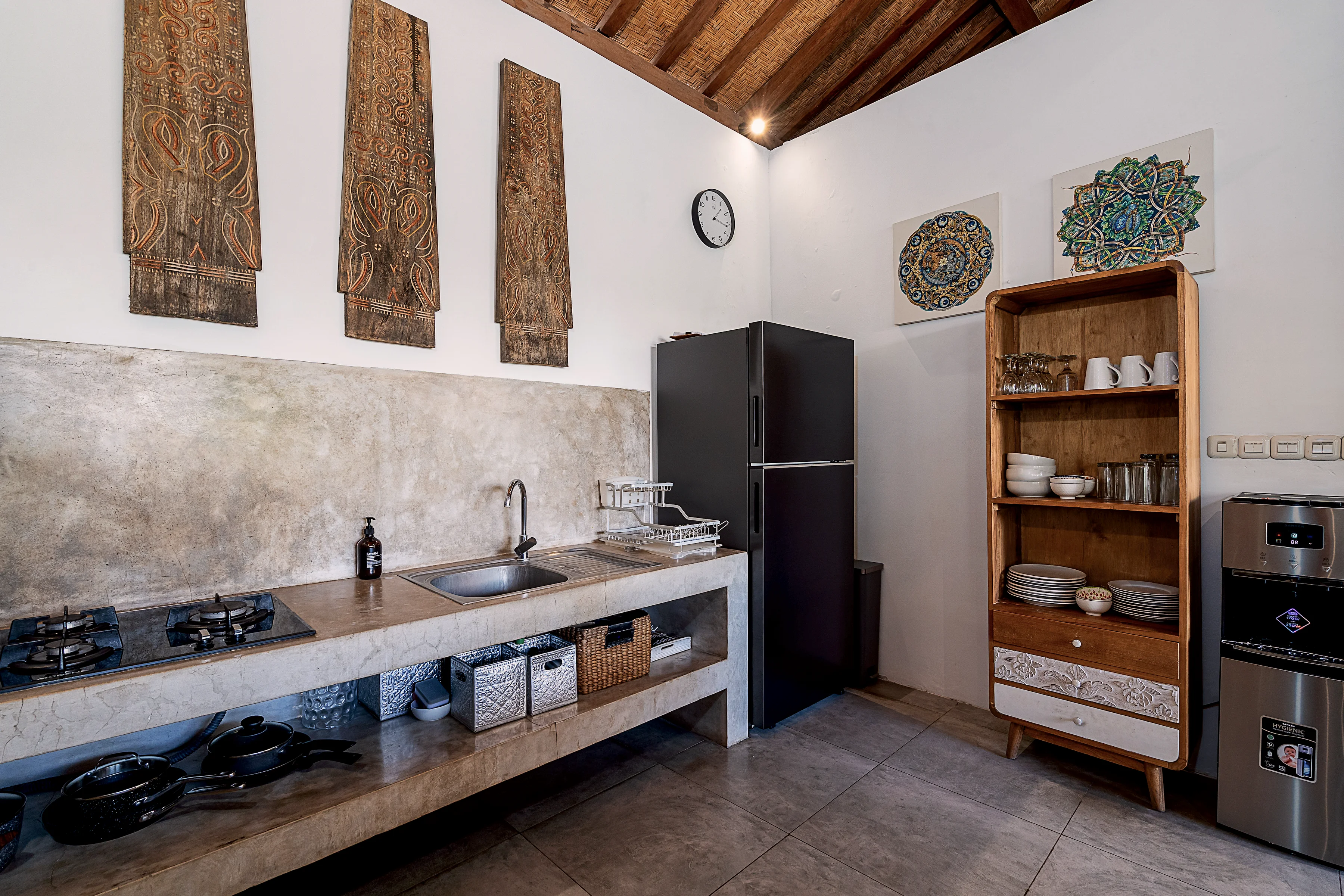 The kitchen with a tall fridge, a shelf of plates and carved panels