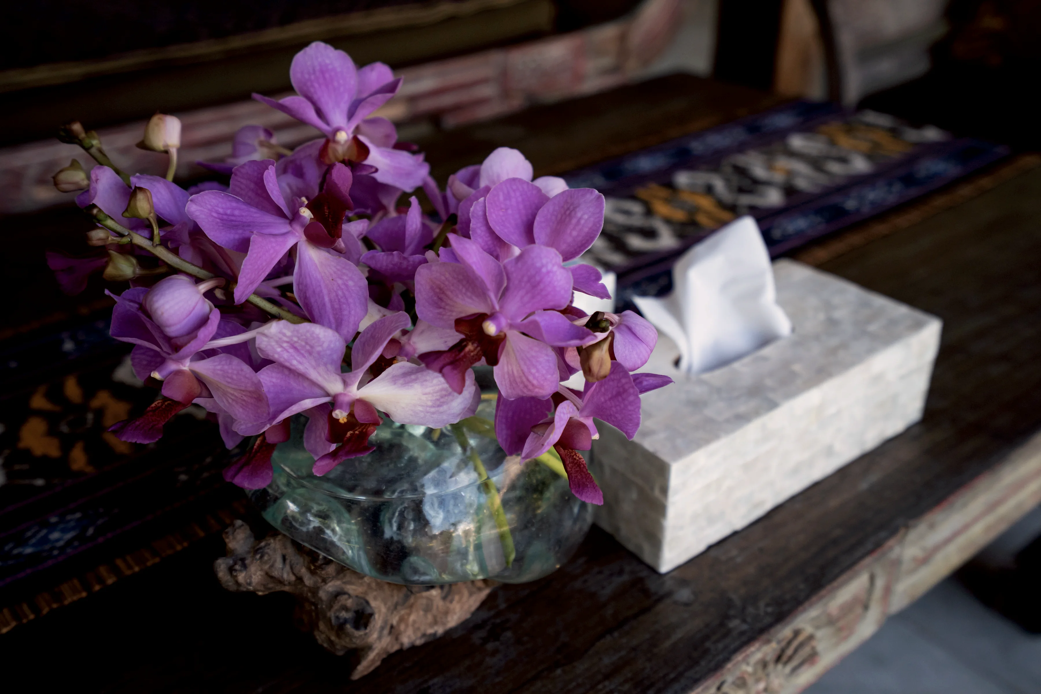 Purple orchids in a glass bowl on a woven table runner