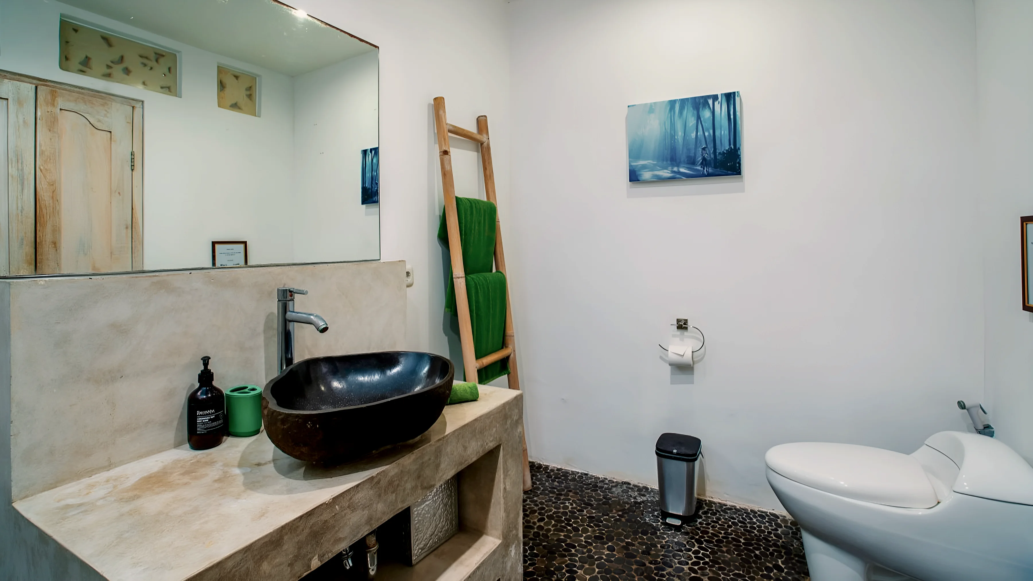 A bathroom with a stone basin, a pebble floor and a towel ladder