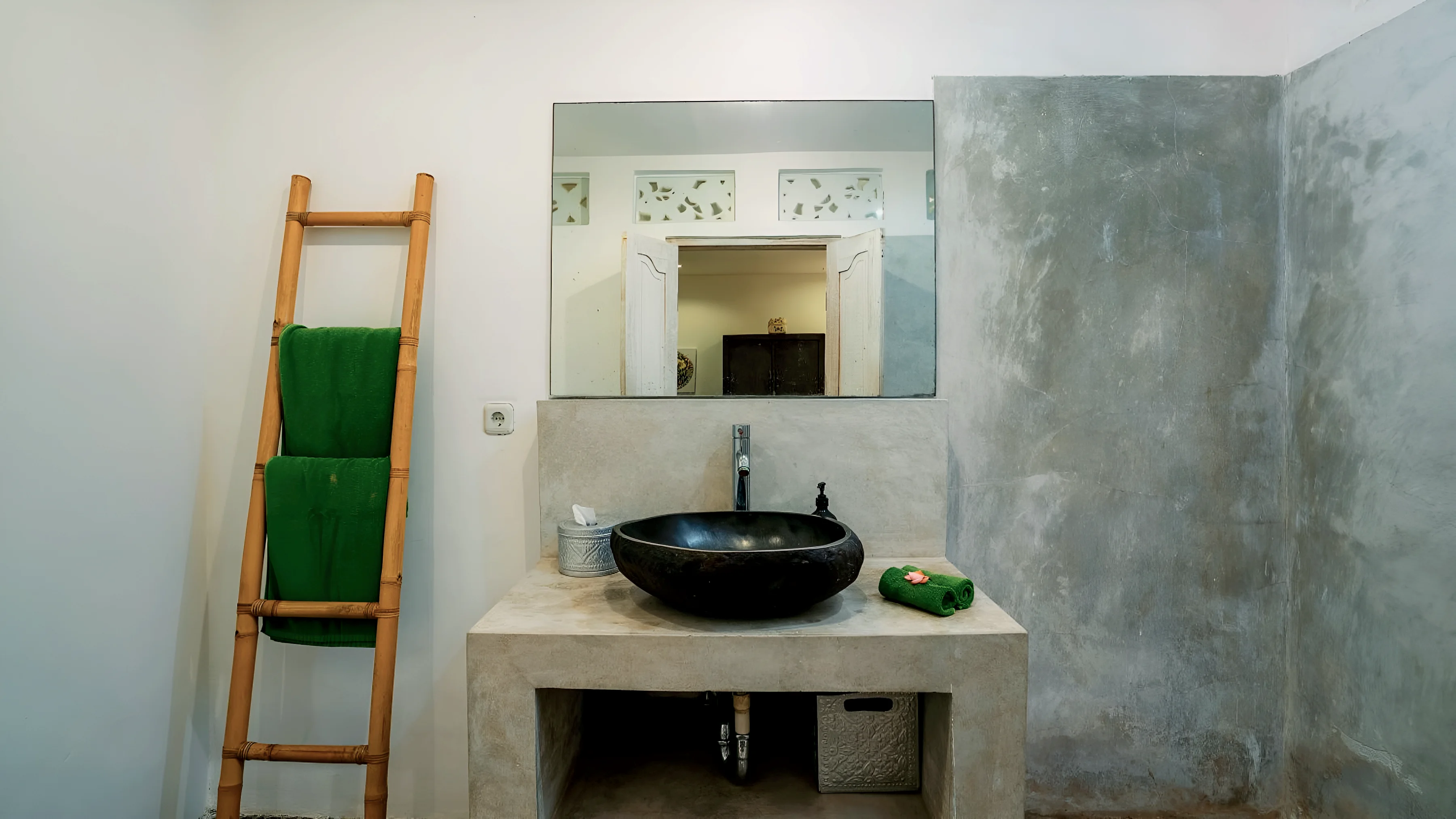 A stone basin on a concrete counter, green towels on a bamboo ladder